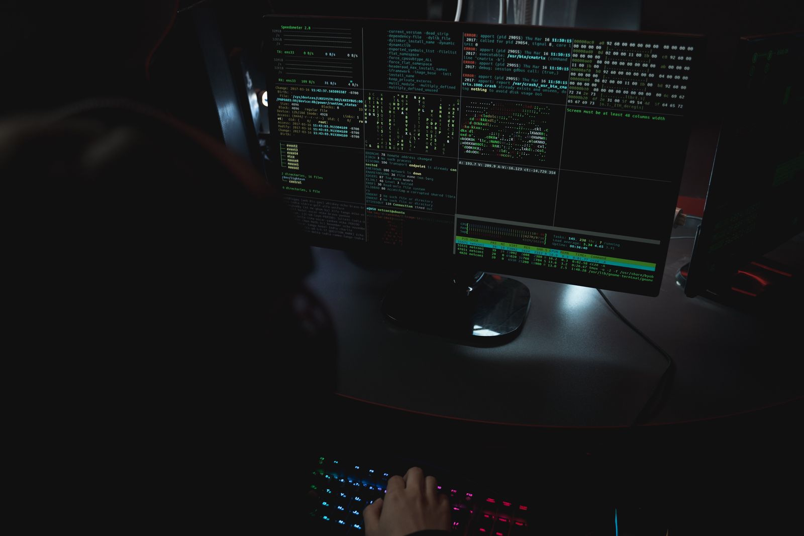 Multiple monitors display code in a dark room used for cybersecurity analysis.