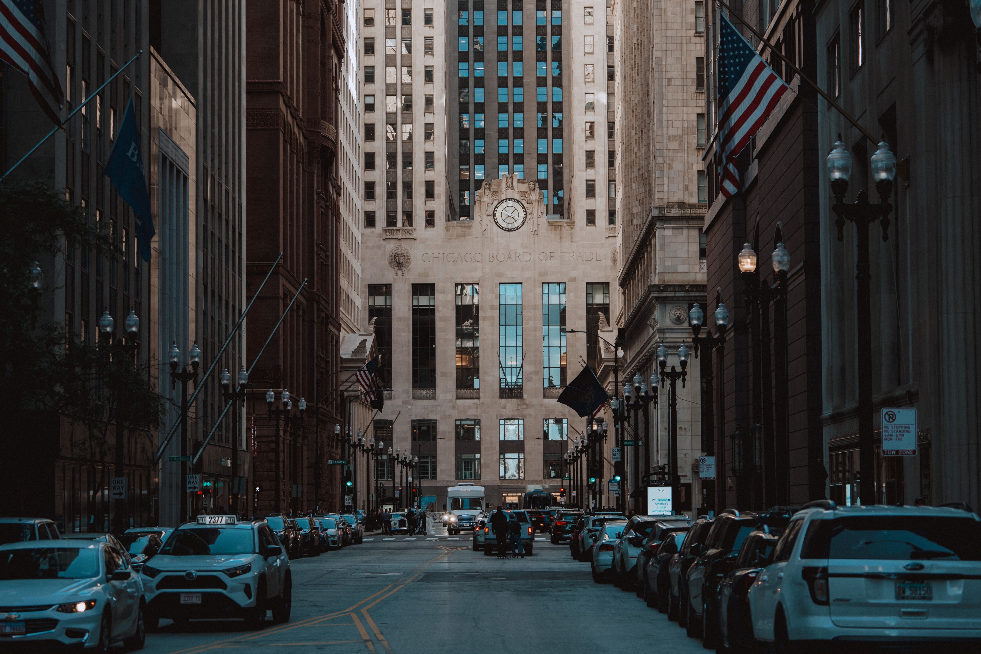Exterior of the Chicago Board of Trade Building, with its stone facade and clock overlooking traffic and American flags along the street.