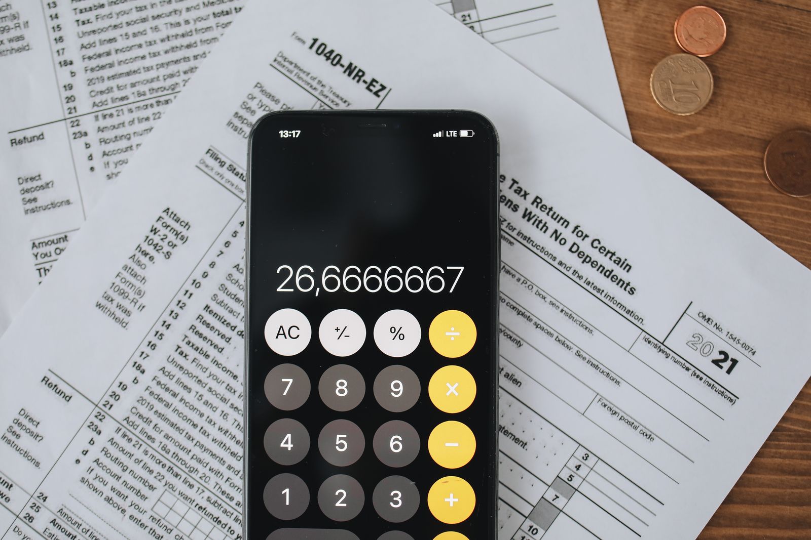 A smartphone calculator resting on US federal tax forms next to a stack of coins, representing digital asset tax reporting