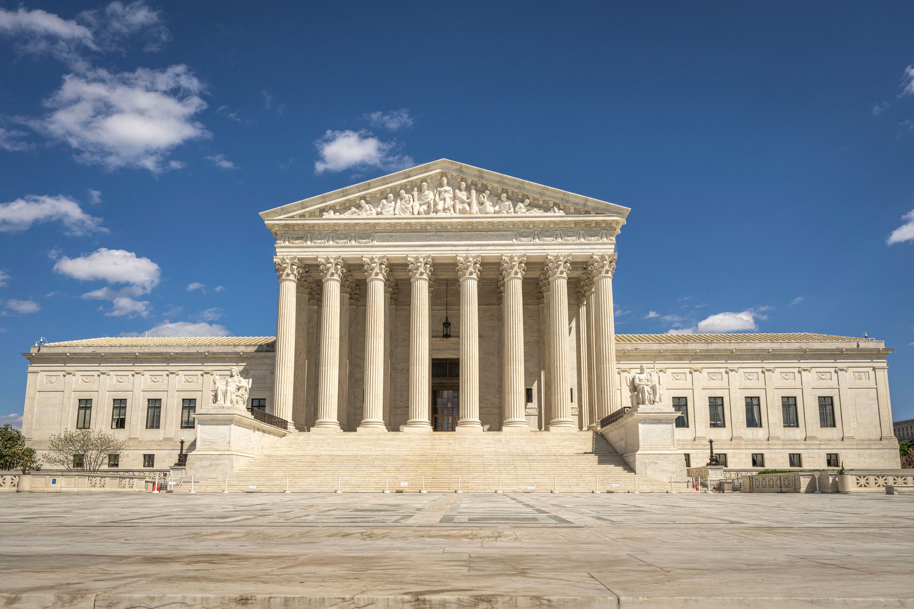 The front of the United States Supreme Court building, with classical columns, marble steps and a sculpted pediment beneath a blue sky.